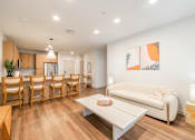 Thumbnail 8 of 9 - A living room with a white couch, wooden chairs, and a painting on the wall.