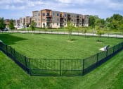 Thumbnail 10 of 36 - a fenced in dog park with an apartment building in the background at Statesman Apartments, Franklin, WI