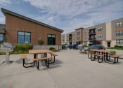 Thumbnail 28 of 36 - an outside patio area with picnic tables in front of an apartment building at Statesman Apartments, Franklin, Wisconsin