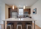 Thumbnail 30 of 36 - an open kitchen with a large island with three stools at Statesman Apartments, Wisconsin 53132