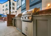 Thumbnail 14 of 52 - a row of barbecue grills on a patio next to a building at Aster Apartments, Beachwood Ohio