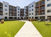 Thumbnail 8 of 22 - Courtyard with green lawn and paver walkway at Timber Club Apartments, St. Peters