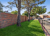 Thumbnail 8 of 44 - a brick retaining wall with trees and a chain link fence at Wellington at Willow Bend Apartments, Plano, 75093