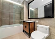 Thumbnail 22 of 29 - A modern bathroom with a white bathtub, wooden cabinet, and a white toilet.