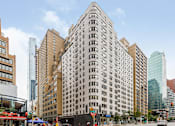 Thumbnail 6 of 6 - A tall building with a lot of windows in the middle of a city street.