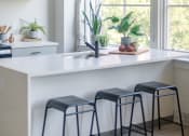 Thumbnail 1 of 42 - a kitchen with a white counter top and three black stools in front of a window at The 22 Apartments, St. Louis, MO 63103