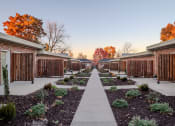 Thumbnail 7 of 11 - a pathway between two rows of brick buildings with plants and trees