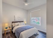 Thumbnail 17 of 27 - A bedroom with a bed, a nightstand with a lamp, and a painting on the wall.