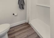 Thumbnail 24 of 27 - A white toilet sits in a bathroom with a grey towel hanging on the wall.