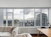 Thumbnail 4 of 13 - A modern living room with a view of the cityscape outside the large window.