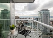 Thumbnail 11 of 13 - A balcony with a chair and a potted plant overlooking a cityscape.