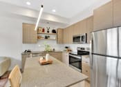 Thumbnail 81 of 107 - A modern kitchen with a stainless steel refrigerator, a wooden cutting board on the island, and a white chair.