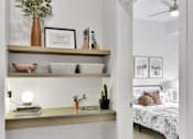 Thumbnail 70 of 107 - A bedroom with a bed, a shelf with decorative items, and a mirror.