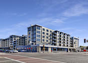 Thumbnail 3 of 107 - A modern multi-story building with a parking lot in front.