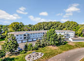 Thumbnail 4 of 13 - A large white building surrounded by trees and a circular garden in front.