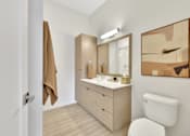 Thumbnail 63 of 107 - A bathroom with a white toilet, a wooden vanity with a mirror, and a brown towel hanging on the door.