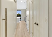 Thumbnail 71 of 107 - A long hallway with white doors and wood floors.