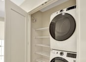 Thumbnail 90 of 107 - A white washing machine is in a small space between a wall and a shelf.
