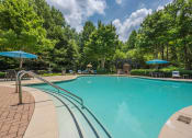 Thumbnail 6 of 34 - a swimming pool with trees in the background and blue umbrellas