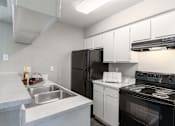 Thumbnail 45 of 46 - A kitchen with a black refrigerator, white cabinets, and a stove top oven.