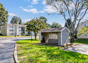 Thumbnail 13 of 25 - A small building sits in the middle of a grassy area with apartment buildings in the background.