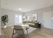 Thumbnail 1 of 15 - A living room with a green couch, a chair, and a potted plant.