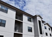 Thumbnail 13 of 15 - the exterior of a multifamily building with a cloudy sky in the background