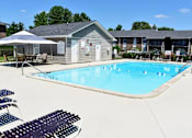 Thumbnail 1 of 24 - A pool with a sun umbrella and chairs in front of a building.