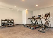 Thumbnail 22 of 24 - A room with a treadmill, a stationary bike, and a bench with dumbbells.