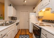 Thumbnail 6 of 27 - A kitchen with white cabinets and appliances, a sink, and a door in the background.