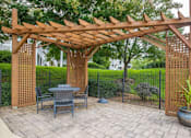 Thumbnail 23 of 27 - A wooden pergola with a table and chairs underneath it.