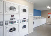 Thumbnail 19 of 31 - A row of white washing machines are lined up in a laundromat.