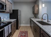 Thumbnail 12 of 38 - A kitchen with a black refrigerator, a microwave above the stove, and a sink with a faucet.