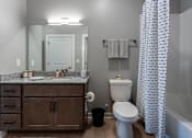 Thumbnail 15 of 38 - A bathroom with a white toilet, a wooden vanity, and a shower curtain.