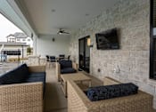 Thumbnail 28 of 38 - A patio with a couch, chairs, and a television mounted on a stone wall.
