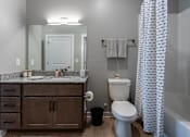 Thumbnail 5 of 38 - A bathroom with a white toilet, a wooden cabinet, and a shower curtain.