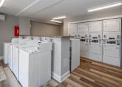 Thumbnail 22 of 25 - A laundry room with a washer and dryer on the left and a row of washers and dryers on the right.
