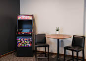 Thumbnail 7 of 21 - A small table with a plant on it sits between two chairs and a video game machine.