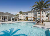 Thumbnail 12 of 28 - A large swimming pool in front of a building with palm trees.