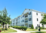 Thumbnail 10 of 28 - A white apartment building with a green lawn in front.