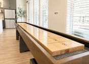 Thumbnail 12 of 22 - A shuffleboard table in a room with a refrigerator and a plant in the background.