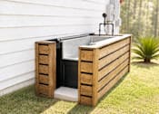 Thumbnail 21 of 22 - A wooden outdoor sink with a faucet is placed on a grassy area next to a house.