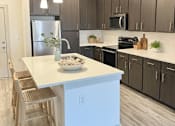 Thumbnail 20 of 28 - A modern kitchen with a white island and wooden chairs.