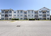 Thumbnail 28 of 28 - A large white apartment building with a parking lot in front.