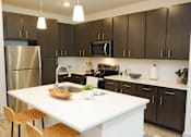 Thumbnail 4 of 28 - A modern kitchen with a white island and dark brown cabinets.