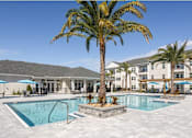 Thumbnail 1 of 28 - A palm tree stands in front of a pool and apartment building.
