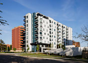 Thumbnail 1 of 28 - A modern multi-story apartment building with balconies and a mix of white and darker colored facades.