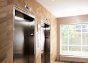 Thumbnail 5 of 28 - Two stainless steel elevators in a hallway with wood paneling on the walls.