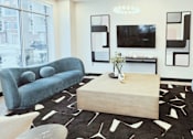 Thumbnail 10 of 37 - A living room with a blue couch, a wooden coffee table, and a black and white rug.