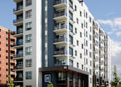 Thumbnail 4 of 28 - A modern apartment building with balconies on the upper floors.